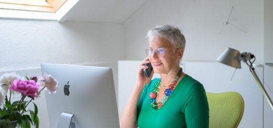 Eveline Bets zit op kantoor, achter haar Imac en belt met een opdrachtgever.